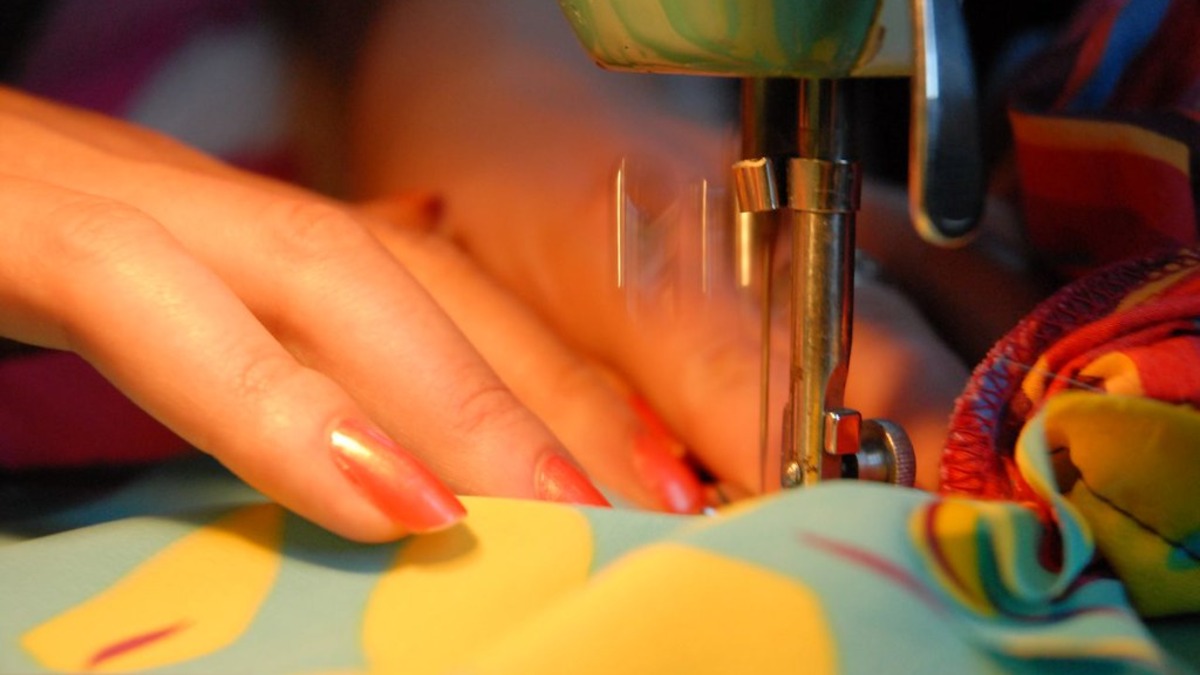 Main guidant un tissu coloré sous le pied d’une machine à coudre