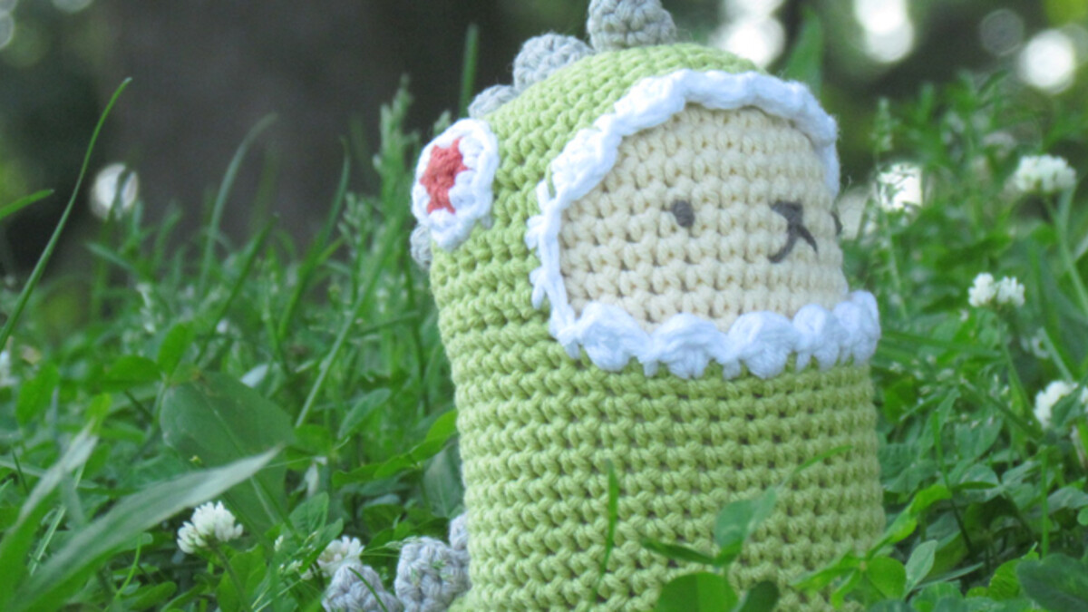 Amigurumi dinosaure vert au crochet posé dans l’herbe